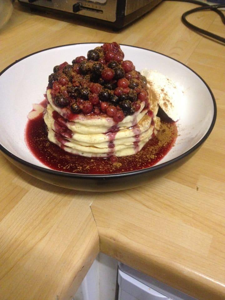 A pancake stack topped with blackcurrants, redcurrants and blueberries in syrup.