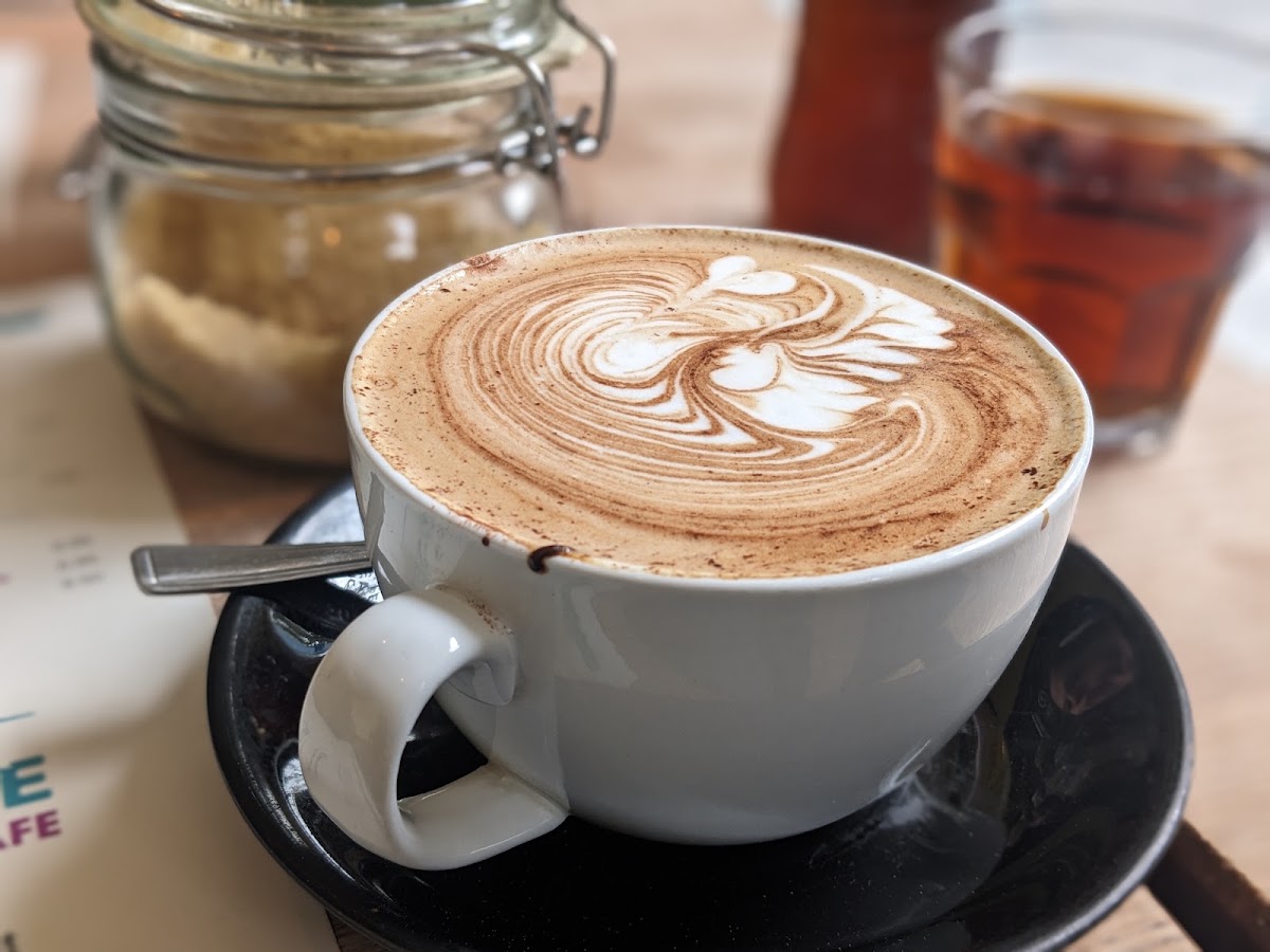 A cappuccino with detailed rosetta latte art beside a jar of demerara sugar.